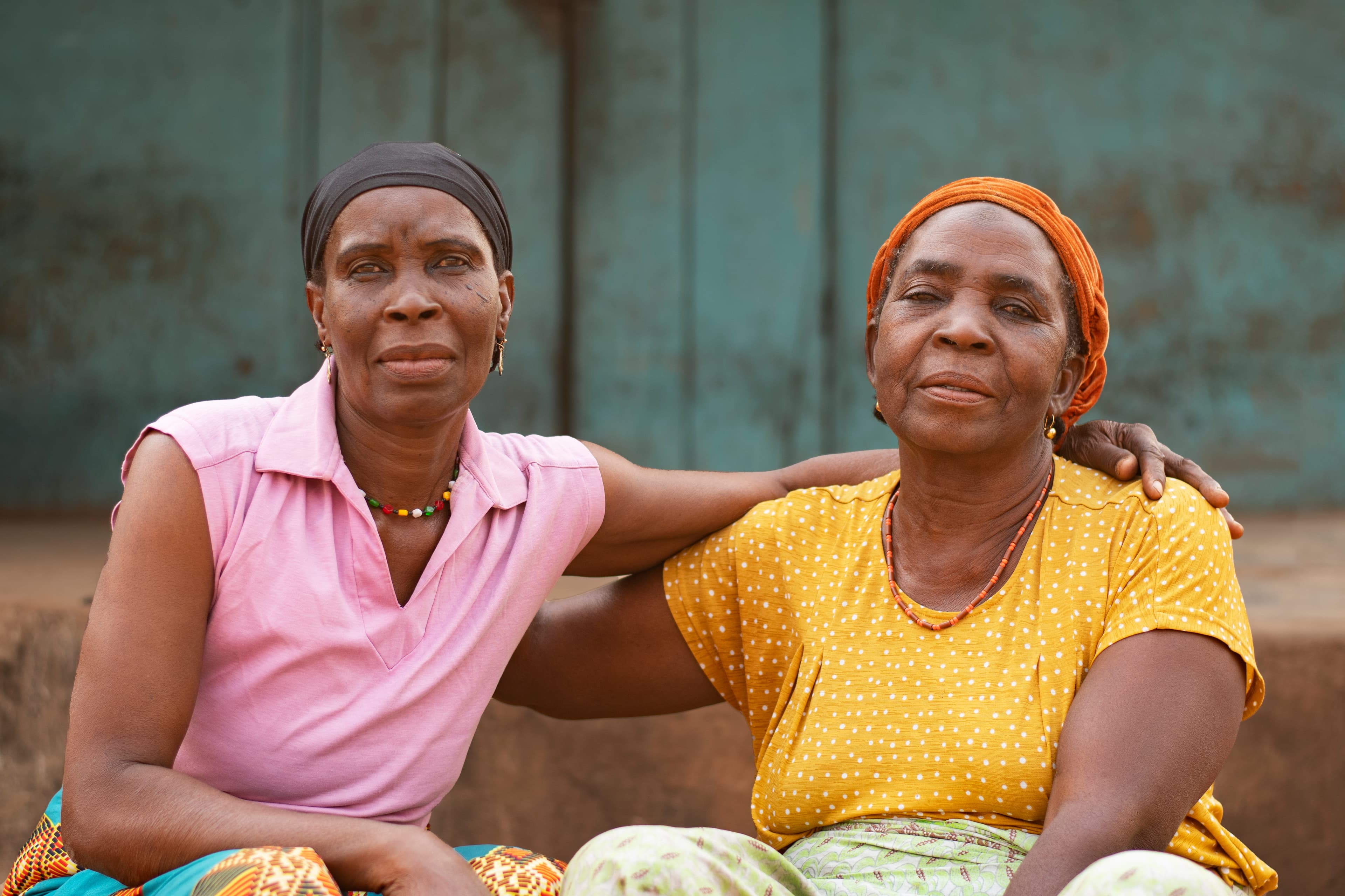 Two older African women seated together with an arm around one another